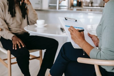 Person writing on clipboard while talking with someone over coffee