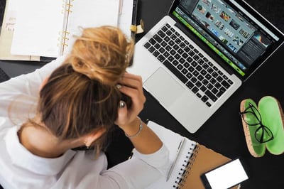 Person sitting with head in hands and working on laptop