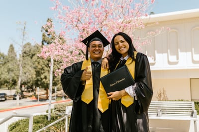 Two graduates smiling and posing with diploma