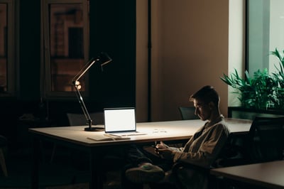 Person sitting on phone in dark room in front of laptop