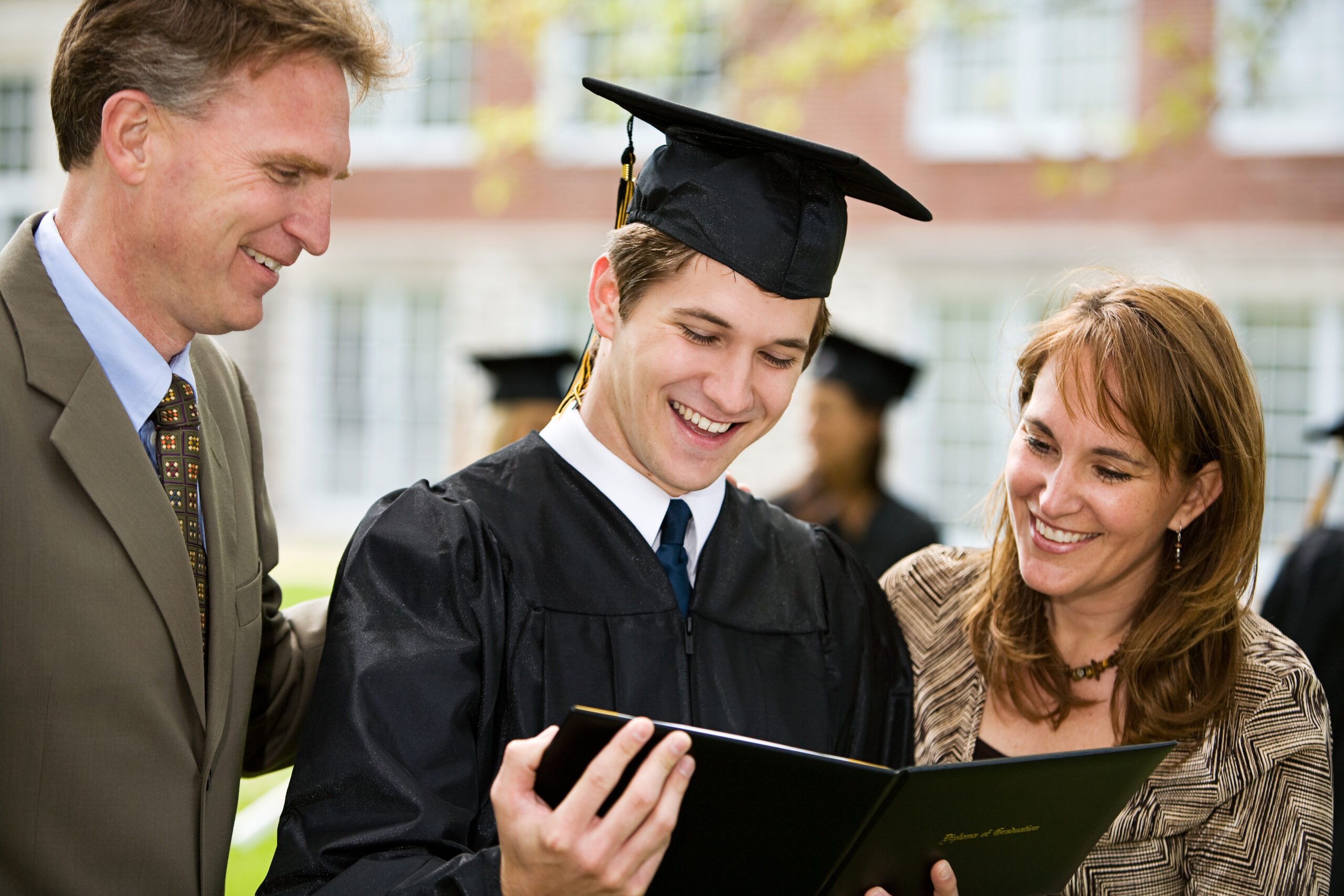 graduate in cap and gown reading card with parents