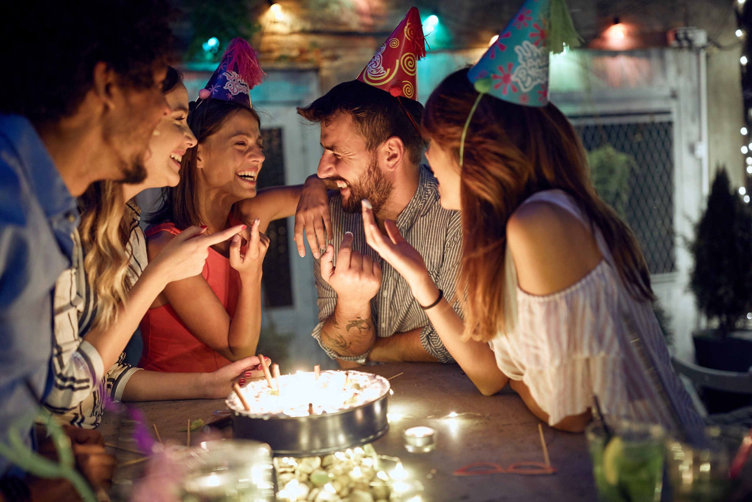 People in birthday hats laughing around a birthday cake