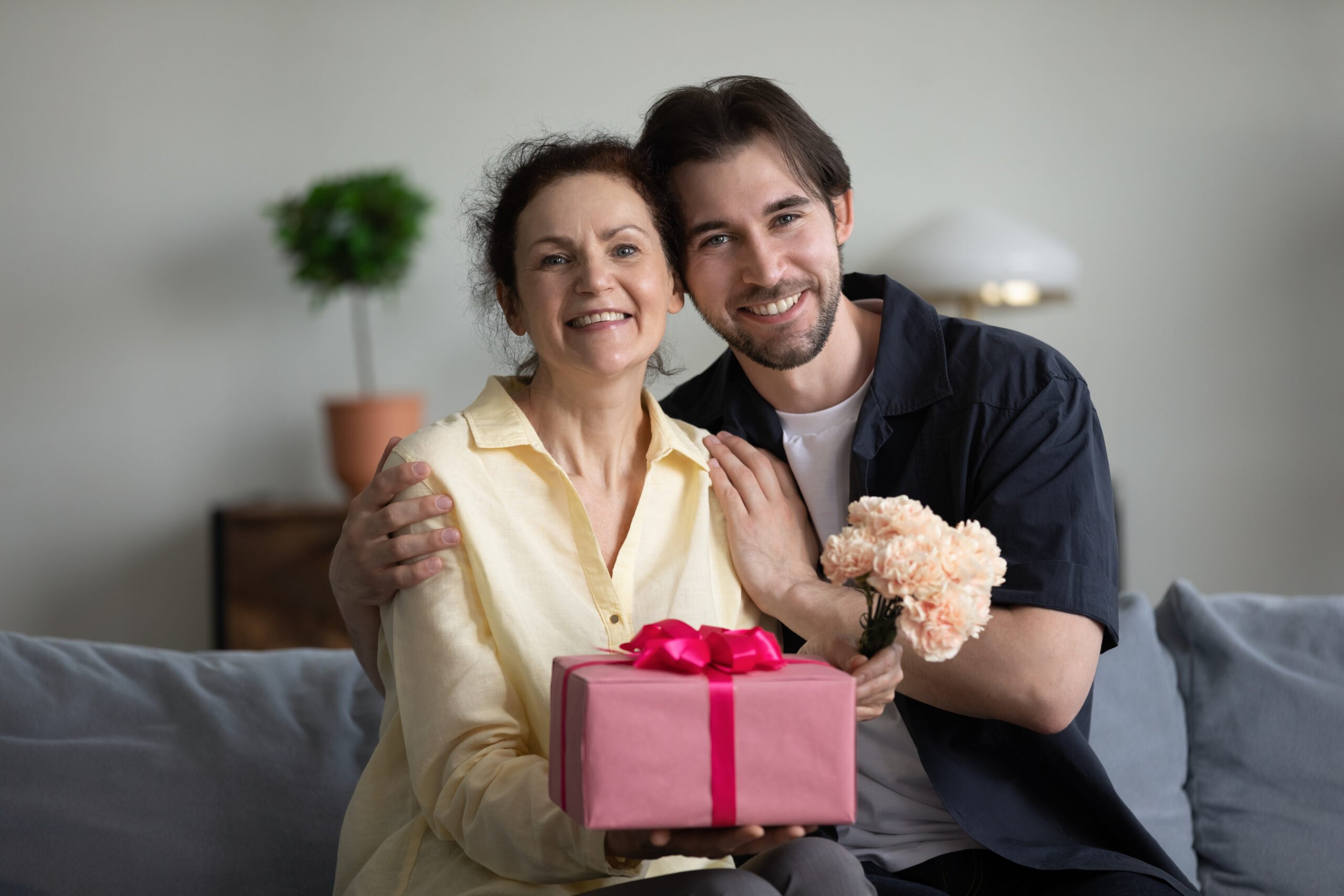 son offering happy birthday mom messages to mother on couch