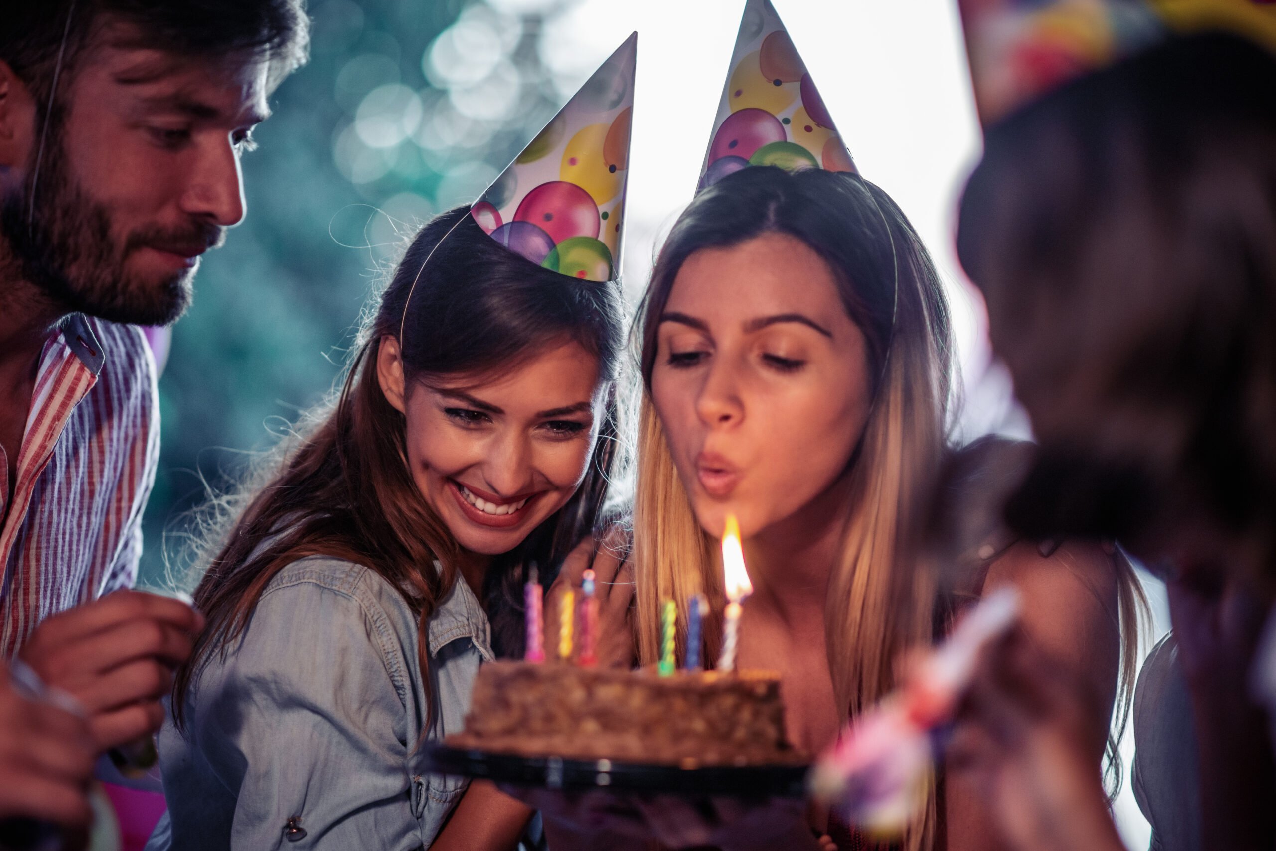 People smiling in party hats while one person blows out a birthday cake